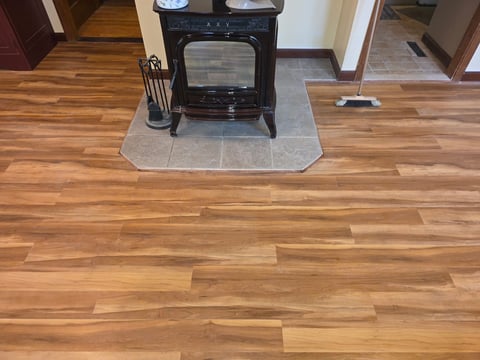 Black wood-burning stove on protective slate hearth with fireplace tools, set on wood plank flooring in home interior