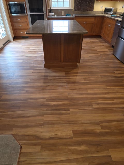 Modern kitchen with wood flooring, dark wood island with gray countertop, and stainless steel appliances