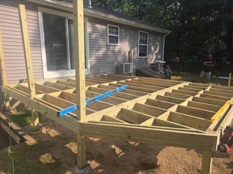 Wooden deck frame under construction with exposed joists and support beams attached to a residential house