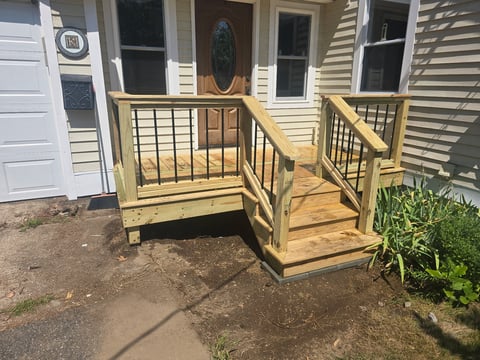 Wooden front porch with metal railing and steps leading to a house entrance with white siding and brown door