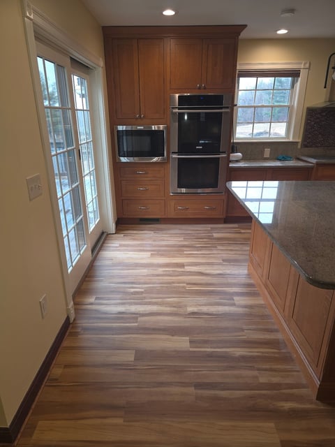 Modern kitchen with wood cabinetry, stainless steel double wall ovens, hardwood flooring, and windows overlooking a wooded view