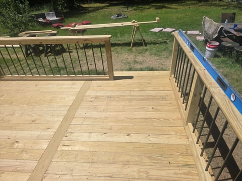 Wooden deck construction in progress with newly installed railings and tools scattered in the yard behind it