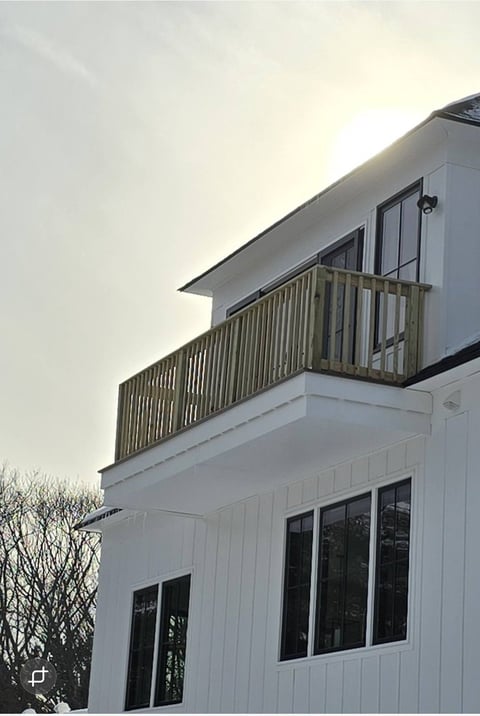 White modern house with metal balcony railing, large black-framed windows, and bare tree branches visible on left side