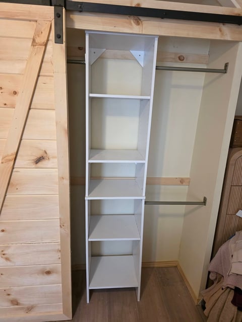 White shelving unit with five shelves inside an open wooden closet with metal hanging rods