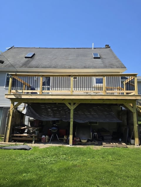 Two-story house with wooden deck and covered porch area beneath, gray roof, green lawn in foreground, clear blue sky